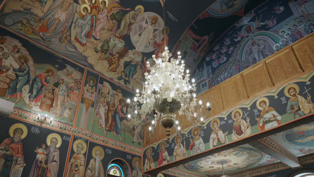 Illuminated Chandelier Hanging Inside Orthodox Church, With Vibrant Frescoes Covering Walls And Ceiling. low angle shot