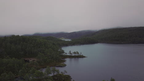 disparo de un dron volando sobre un lago y un bosque en noruega cubierto de niebla y neblina