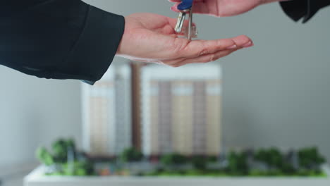 close up moment of hand stretched forward to receive key symbolizing property handover or new ownership with blurred background of building miniature enhancing context of real estate transaction