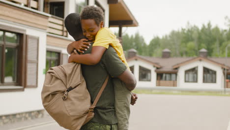 back view of an military father holding and embracing his son outside home