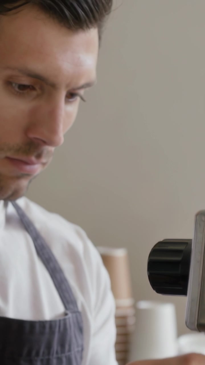Video verticale: Barista con grembiule che blocca il portafiltro, prepara la macchina del caffè al bar per un espresso, con spazio per il testo.