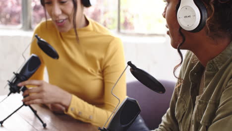 recording podcast at home, multiracial female colleagues wearing headphones, having conversation