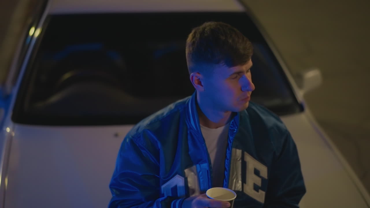 Driver gazes afar, White male driver looks into distance, Cool cinematic scene featuring reflective male driver, Quiet plaza setting with male driver holding paper cup and contemplating