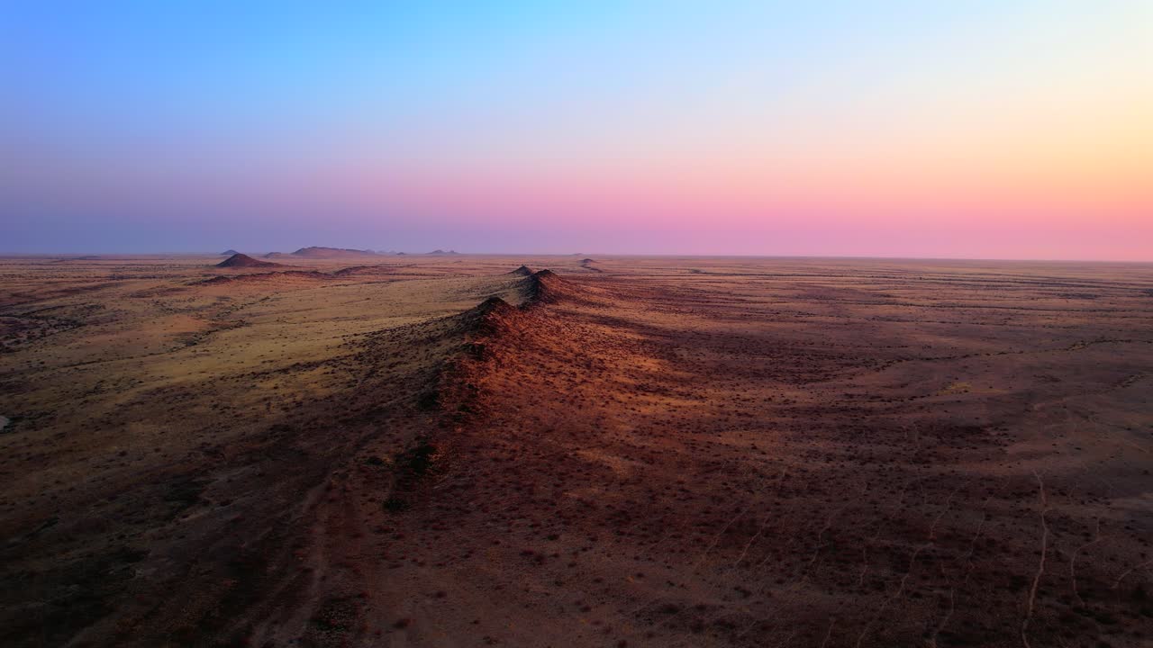 Narrow desert ridge casting long shadows across flat terrain under colorful sky near Spitzkoppe, Namibia