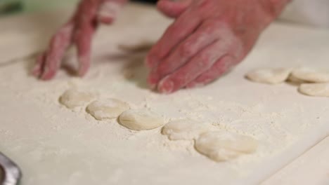 chef flattens a ball of dough using his palms on a floured countertop