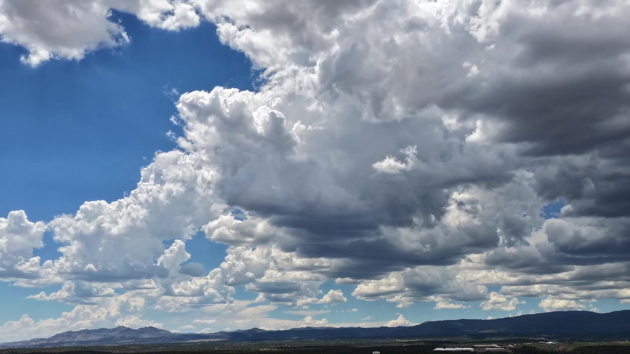 Timelapse 4K da drone di drammatica attività climatica nell'alto deserto. Imponenti nuvole cumuliformi con basi scure e pesanti si muovono aggressivamente sopra le montagne distanti e la macchia arida.