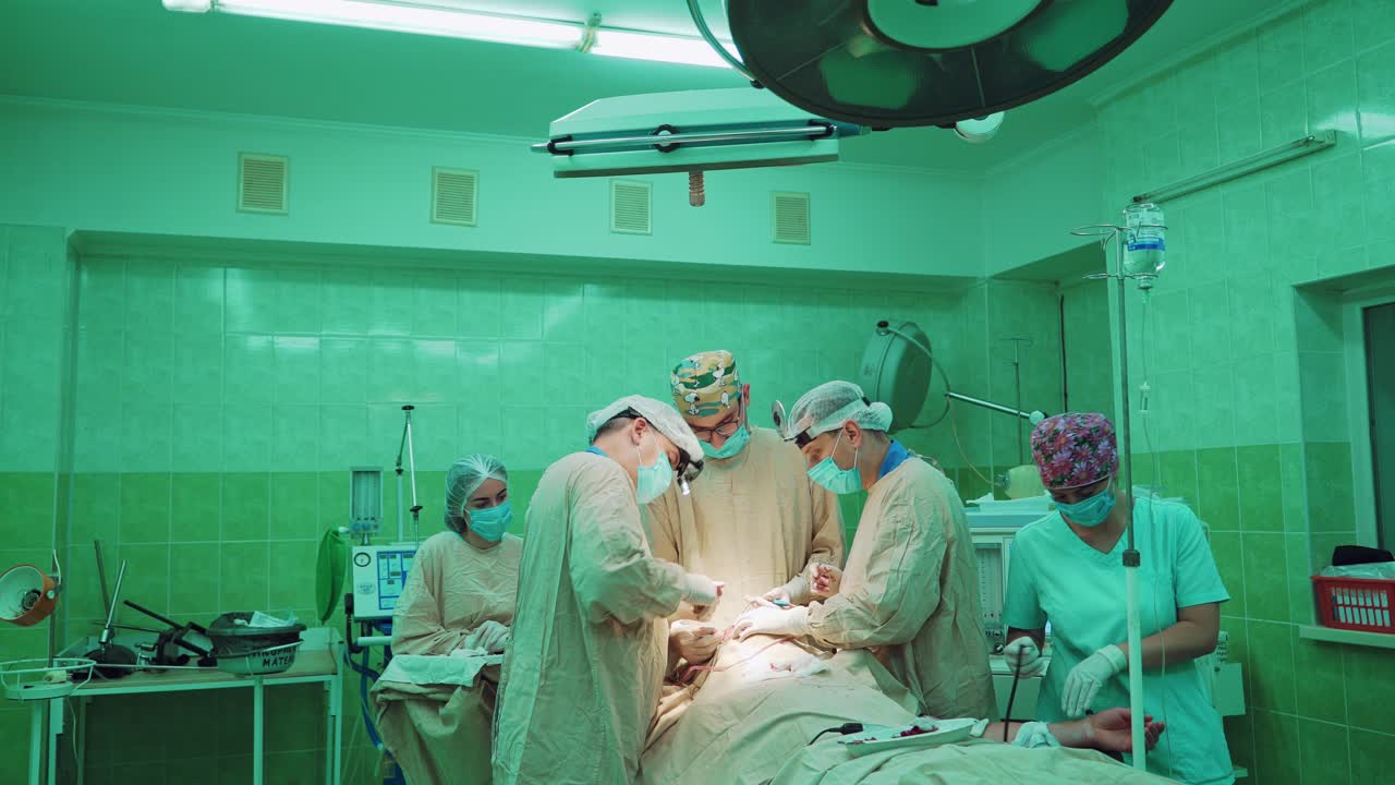Male surgeons and assistants women during the operation in clinic. Doctor's team wearing medical uniform and masks performing operation in hospital operating theater on patient.