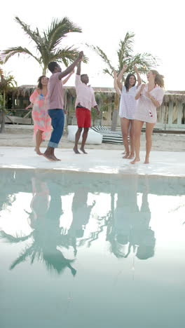 Vertical video of happy diverse group of friends dancing at pool