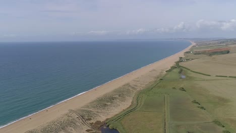 Aerial-tracking-forward-high-above-Chesil-Beach-at-Abbotsbury-looking-along-the-coastline-to-the-west