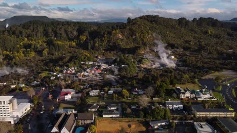 Geothermal-Valley-Te-Puia-with-steaming-hot-pools,-geyser-and-historic-living-Maori-village,-Rotorua,-New-Zealand---aerial-drone