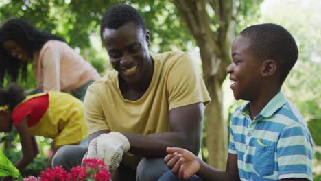 Animation-Eines-Glücklichen-Afroamerikanischen-Vaters-Und-Sohnes,-Der-Blumen-Im-Garten-Pflanzt