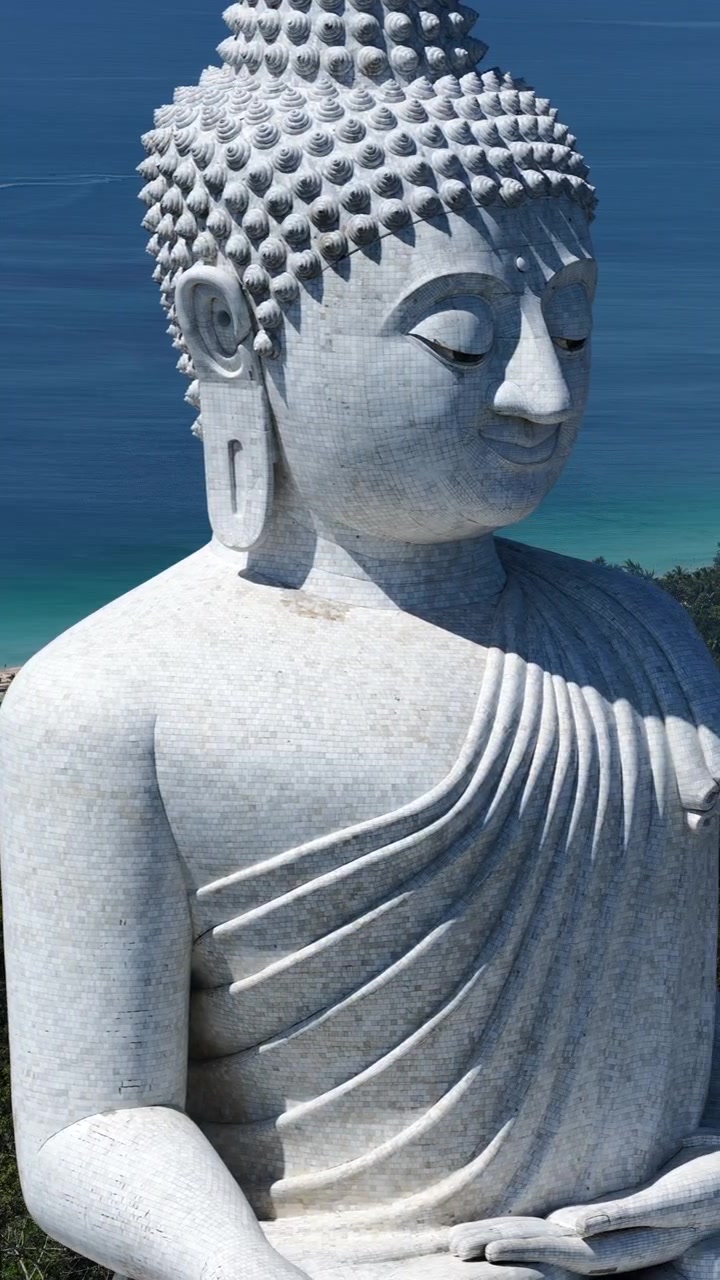 Il Grande Buddha di Phuket riempie l'inquadratura in dettaglio, sullo sfondo del profondo Mar delle Andamane, con una ripresa aerea che si muove verso destra