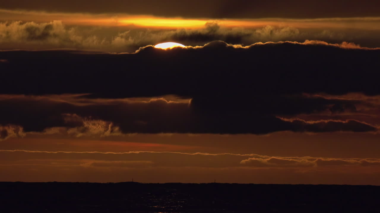 Die Sonne verschwindet hinter dunkelschwarzen Wolken vor einem orangefarbenen Himmel