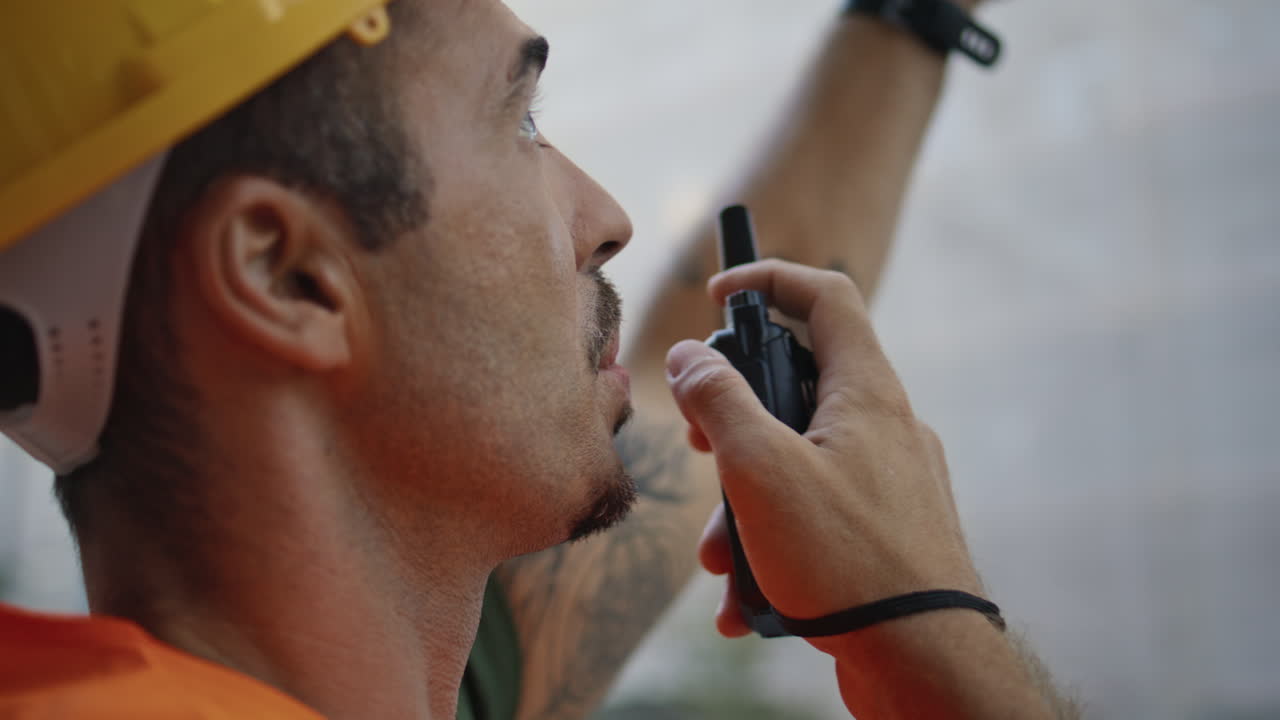 Serious foreman speaking wireless communicator at downtown closeup. Man uniform