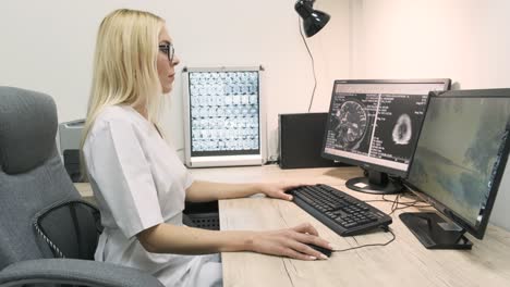 professional female doctor radiologist examines brain ct or mri scan results, working on a computer screen at her personal desk at hospital