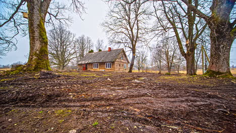 Time-lapse-shot-of-lonely-wooden-forest-house-on-farm-and-excavator-digging-field-in-garden---Working-outdoors-during-autumn-day