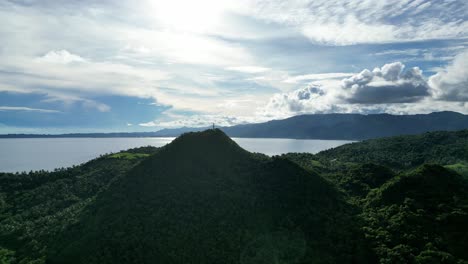 epische, hochwinkelige drohnenaufnahme eines üppig bewaldeten berges mit einem leuchtturm auf der spitze und blick auf eine majestätische wolkenlandschaft und unberührtes meerwasser