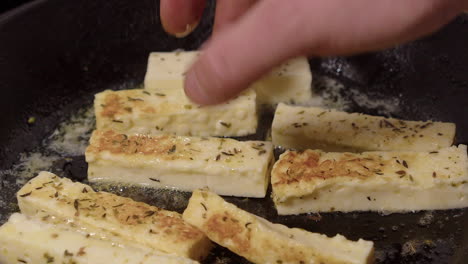 Closeup-fingers-flip-herb-cheese-pieces-in-hot-buttery-cast-iron-pan