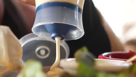 person pouring mayo on a meal