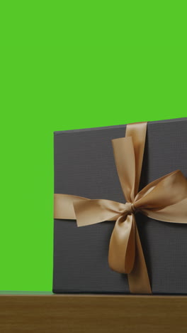 vertical video of present in gift wrapped box decorated with ribbon on table shot against green screen