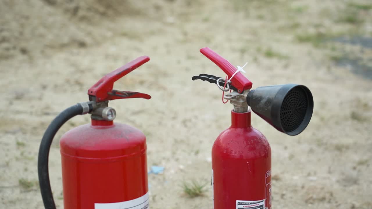 Two red fire extinguishers placed on a sandy surface, ready for use in fire safety training