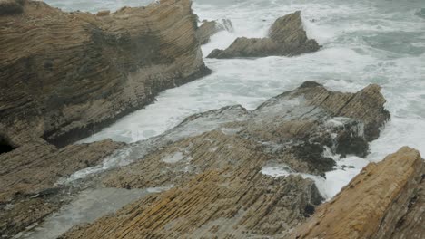 UHD-ocean-view-of-waves-crashing-into-coastal-bluffs-on-overcast-summer-day