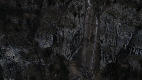 rising drone clip of high mountain waterfall showing steep rock face and water's edge at base of cliff