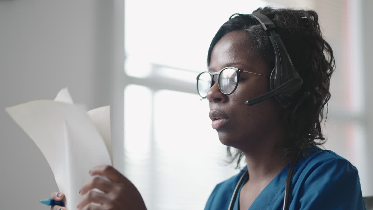 African american black female general practitioner in white coat sitting at desk in doctor's office and scrolling computer mouse while reading patient's medical history