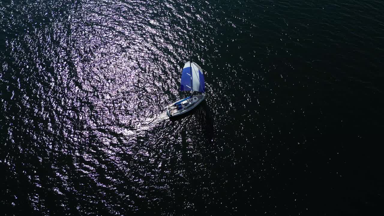 vista aérea de un velero que navega en las aguas oscuras del mar báltico, toma estática de un dron, escena de alto contraste, vela azul