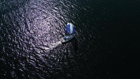 aerial view of a sailboat sailing on the dark water of the baltic sea, static drone shot, high contrast scene, blue sail