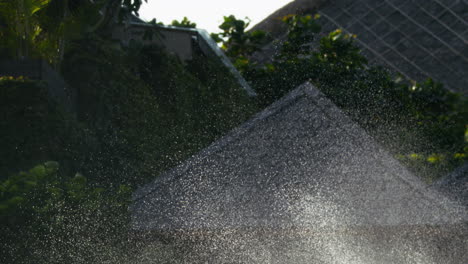 Super slow motion of water spray arcing from lawn sprinkler, mist glows in sunlight