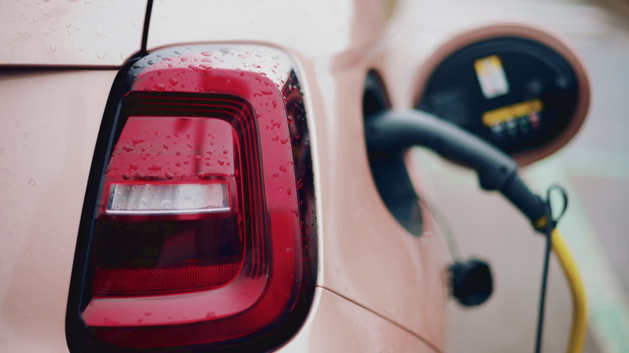 Close up of a pink, electric car charging outdoors under rain