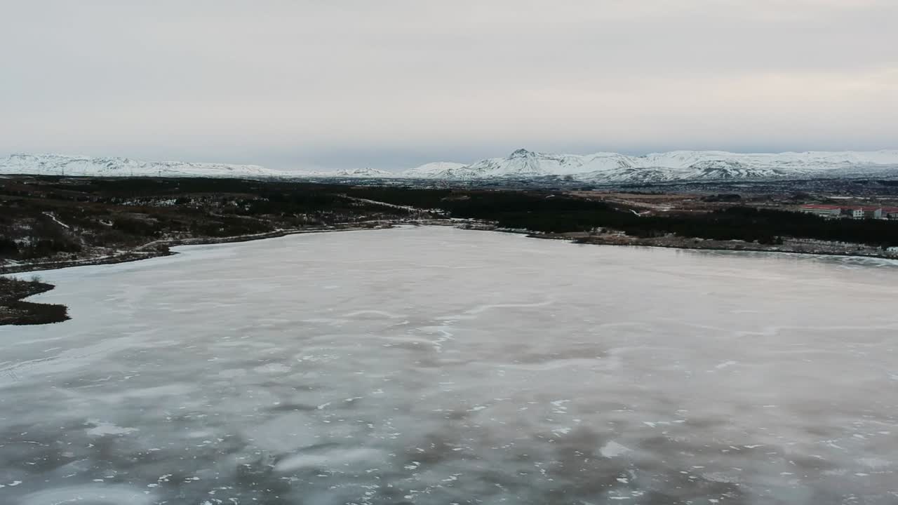 Extreme wide drone shot of  frozen lake Raudavatn, near Reykjavík, Iceland.Vast monochrome expanse of ice with mountains in the distance