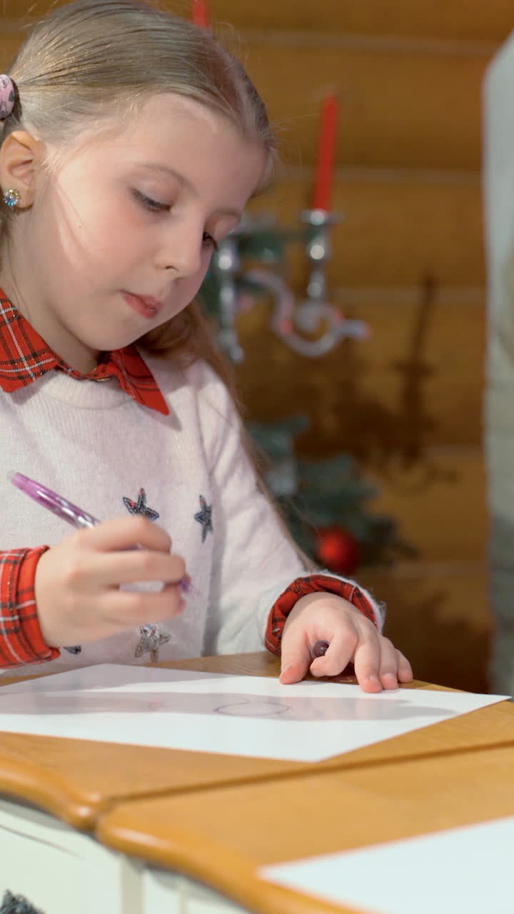 Little girls draw at the table near the fireplace and the Christmas tree. Vertical video