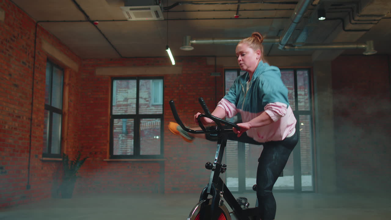 여성은 시 ⁇ 레이터, 사이클 트레이닝에서 유산소 지구력 훈련 운동 심장 루틴을 수행합니다.