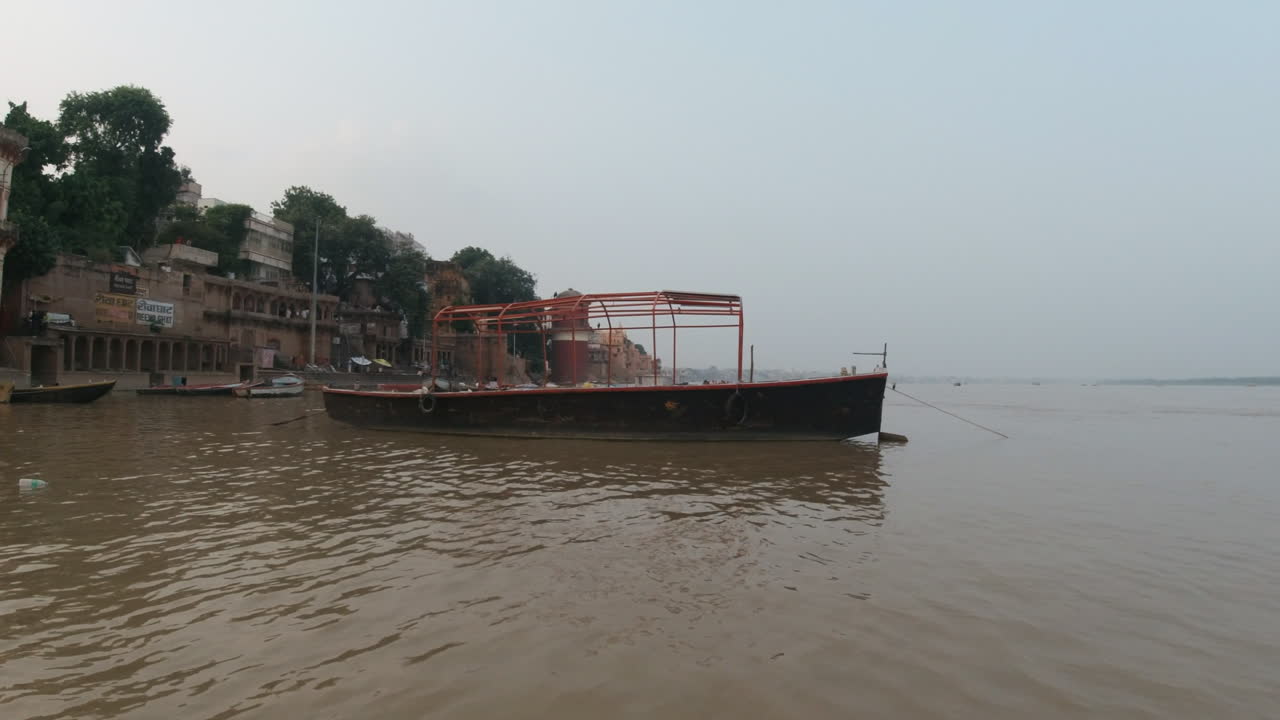 Cinematic sunset scenic boat pan right Ancient Holy city Varanasi India Ganges River canal boat cruise Northern State people at Ghat Pradesh Province landscape gray cloudy