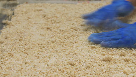 a worker distribute crumble mix over a large tray using a rolling pin