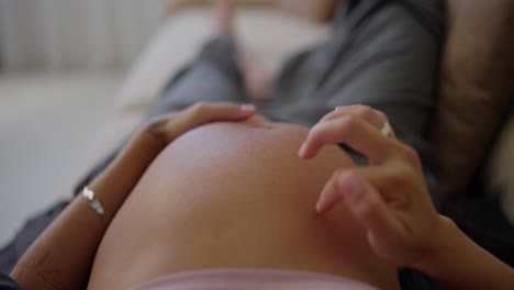 Top-view-close-up-of-happy-pregnant-woman-stroking-her-belly-with-fingers-and-gentle-touches-while-lying-on-sofa-at-home