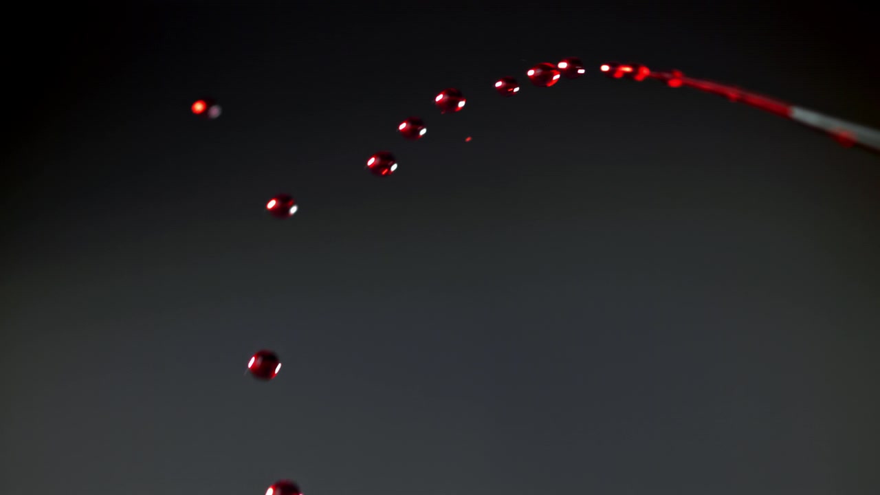 Slow Motion Red Liquid Drops Falling Against a Dark Background