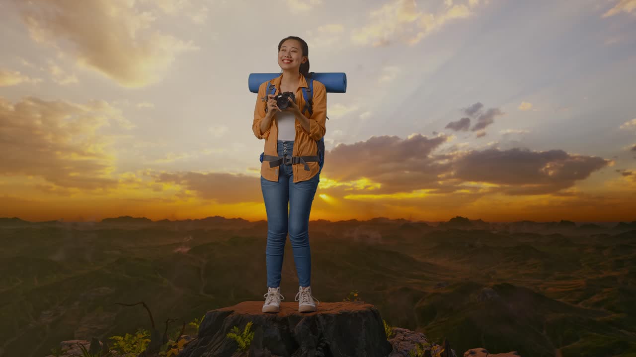 cuerpo lleno de excursionista femenina asiática con mochila de montañismo sonriendo y sosteniendo una cámara en sus manos luego mirando a su alrededor mientras estaba de pie en la cima de la montaña durante la hora del atardecer