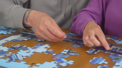 close up of couple sitting at table at home with glass of wine doing jigsaw puzzle together