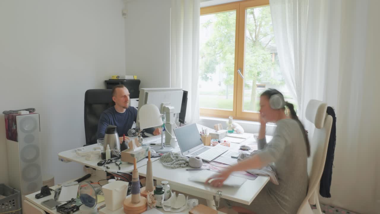 Timelapse capturing the movement and focus of two people working on computers in a bright, cozy room.