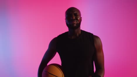 Nahaufnahme-Eines-Studioporträts-Eines-Männlichen-Basketballspielers,-Der-Den-Ball-Vor-Rosa-Beleuchtetem-Hintergrund-Dribbelt-Und-Hüpft-4