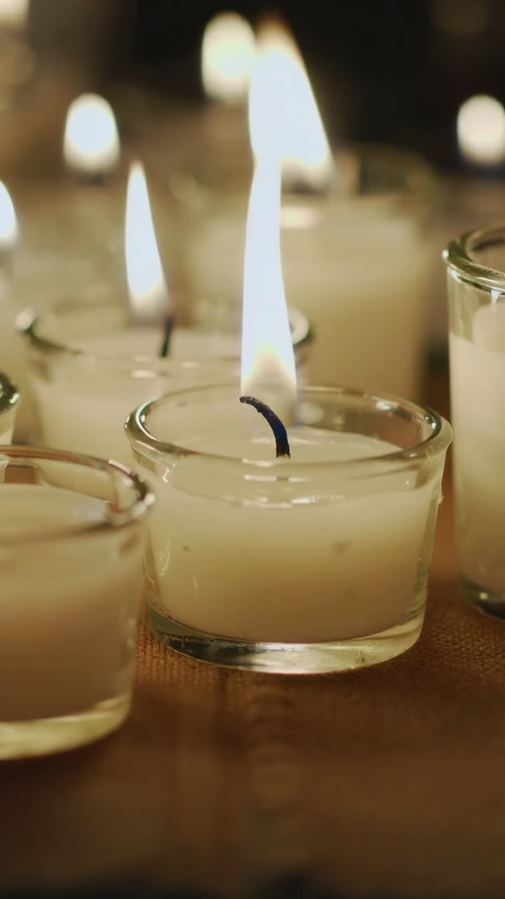 Vertical video: Flickering central glass votive burnt wick bending and wax pooling on wood table