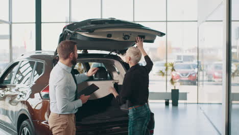 vendedor de automóviles y cliente comprobando el maletero de un suv en una sala de exposiciones