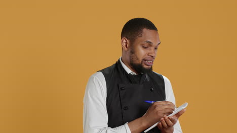 skilled waiter with apron takes meal orders from clients on a notebook