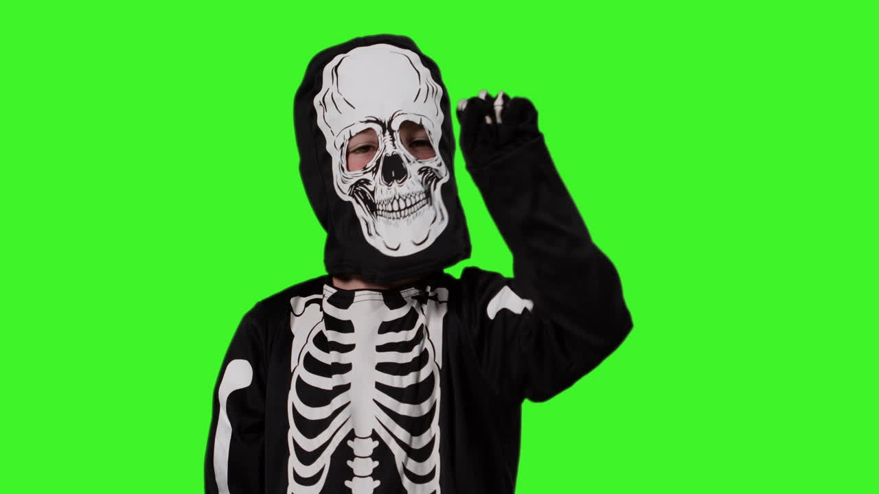 niño vestido con disfraz de esqueleto llamando a la puerta truco o tratar en halloween con cubo en forma de calavera contra la pantalla verde del estudio