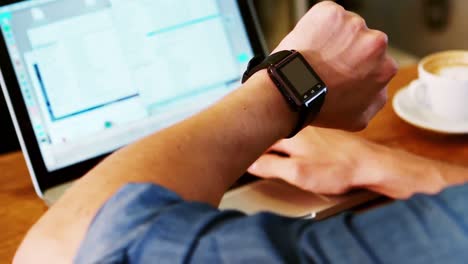 hombre comprobando la hora en su reloj de muñeca mientras usa una computadora portátil