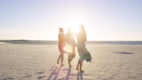 Three-girl-friends-wrapped-in-towels-keeping-warm-on-windy-beach