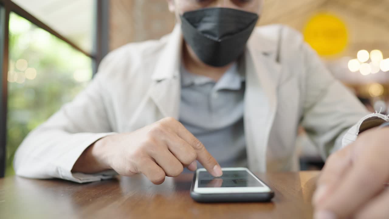 un joven empresario con una máscara quirúrgica está tomando una videoconferencia con los clientes a través de un teléfono inteligente conectado a internet.